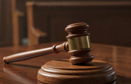 Judge’s gavel rests on a wooden surface with blurred scales of justice and chair in the background