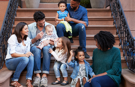A group of adults and children sitting together on outdoor stone steps.
