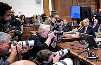 multiple press photographers take pictures during a court proceeding